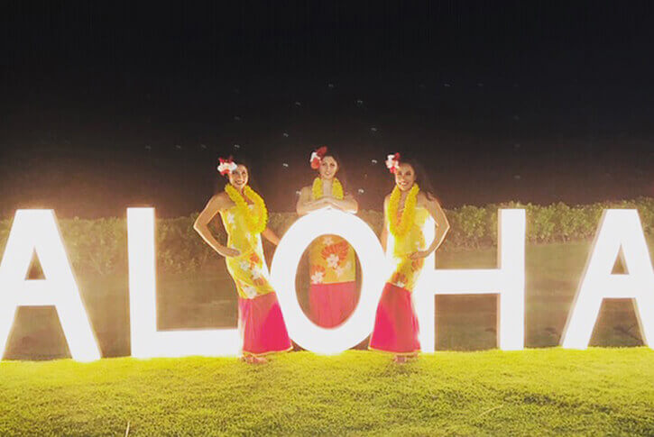 hula dancers posing in front of aloha illuminated sign